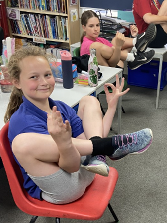 two children sitting in yoga positions on chairs in class and smiling at the camera