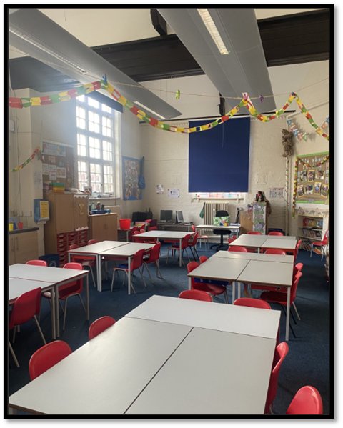 a bright, airy, empty classroom with light grey desks and red chairs