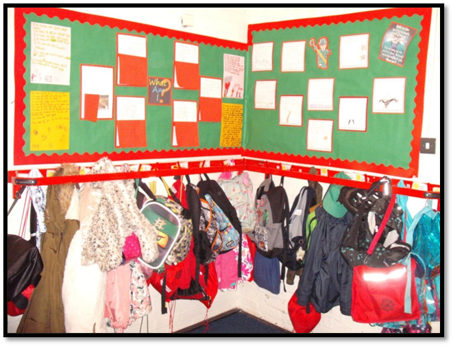 childrens coats and bags hanging on pegs in a school cloakroom