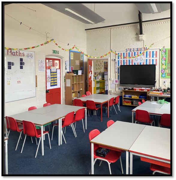 a bright empty classroom with light grey desks and red chairs. There are displays on the walls