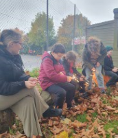 children sitting on logs outside, surrounded by fallen leaves